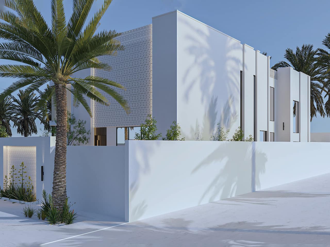 جدار سور أبيض مصمت وكتل بيضاء خلفه تحت شمس قوية يمرّ عليها ظل نخلة، وشريط بنقش مثقّب في أعلى الكتلة، ونخلة وشجيرات قليلة عند قاعدة الجدار.